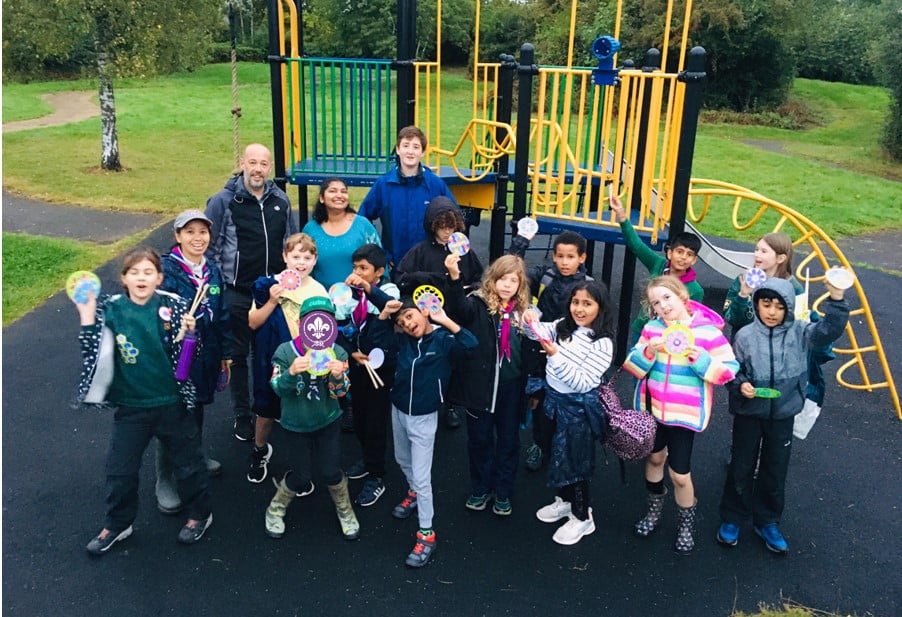 Group photo of 26th Milton Keynes Coniston Cub Scouts group in front of a play park. Everyone is holding a Rangoli craft that they have made in their hand.