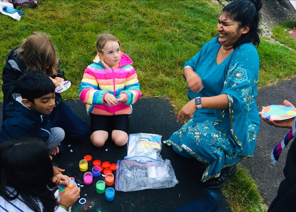 Photo of Cubs sitting down to complete Rangoli sand craft and Cub leader Sital laughing.